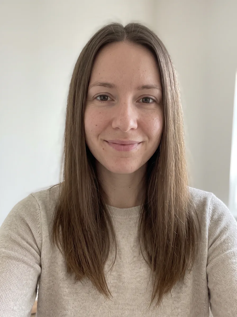 A selfie of a woman with long, straight brown hair parted in the middle, in an oatmeal knit top