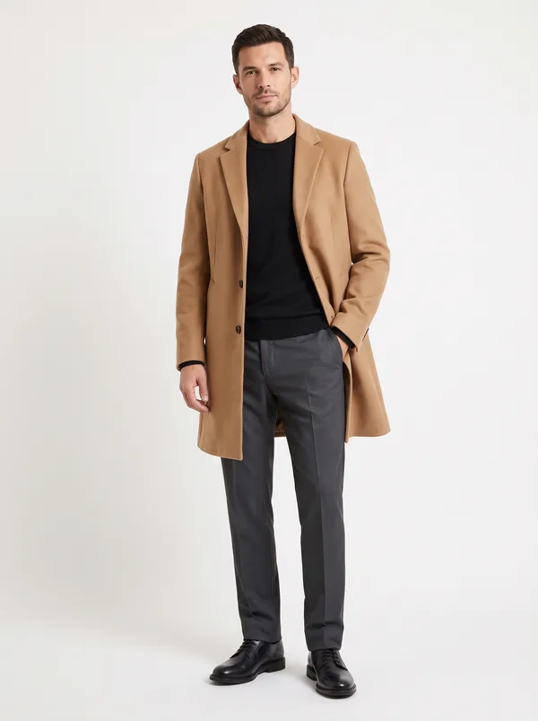 A catalog photo of a camel knee-length overcoat worn open over a black sweater and charcoal trousers